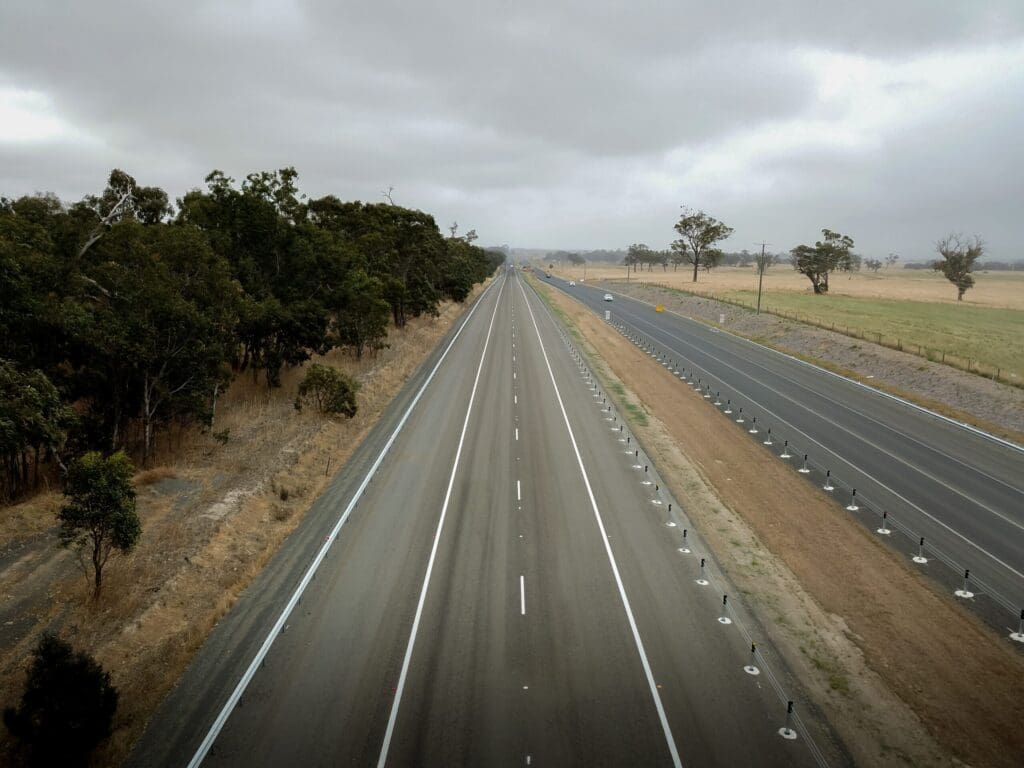 Aerial view of VicRoads Princes Highway with multiple lanes, roadside trees and farmland