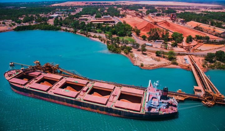 Bulk carrier ship being loaded with red ore at Amrun port facility beside turquoise water