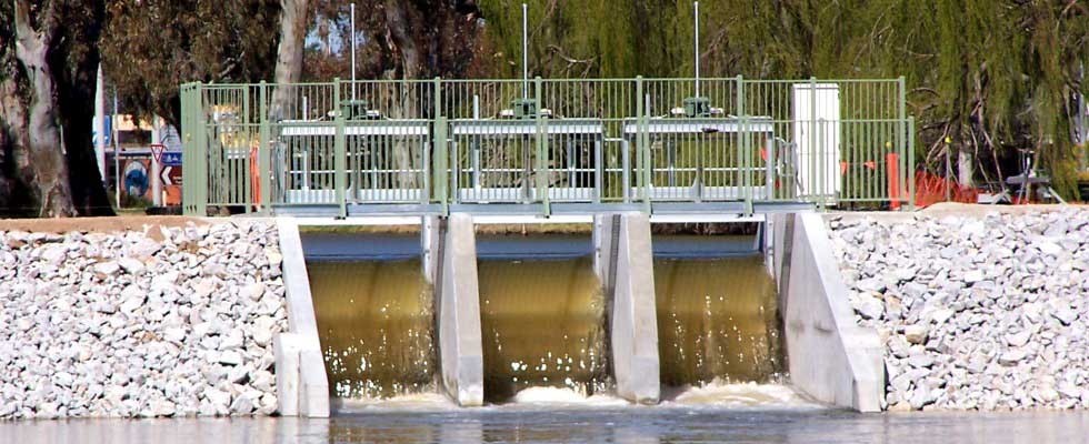 Water flowing through Cohuna Weir gates with green railings, concrete supports and rock embankments