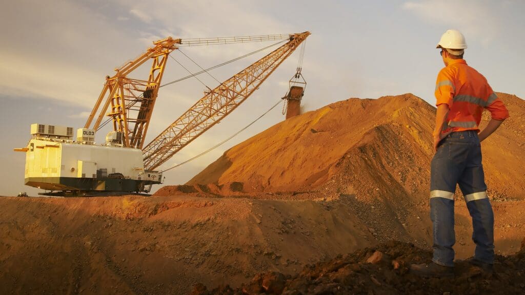Mine worker watching a dragline excavator move material beside a large coal stockpile