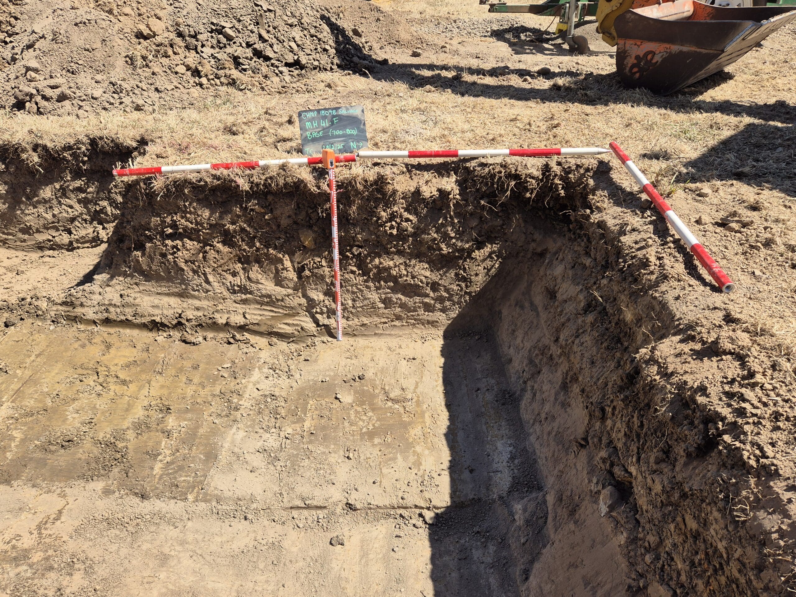 ACHM archaeological test pit with exposed soil profile, measuring rods and site marker board