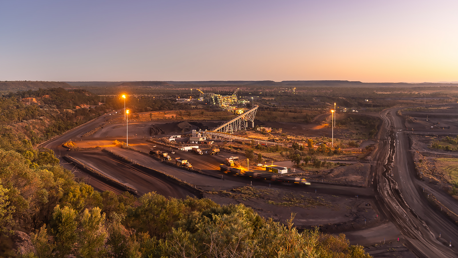 Glencore mining site at dusk with illuminated conveyor infrastructure, haul roads and vehicles