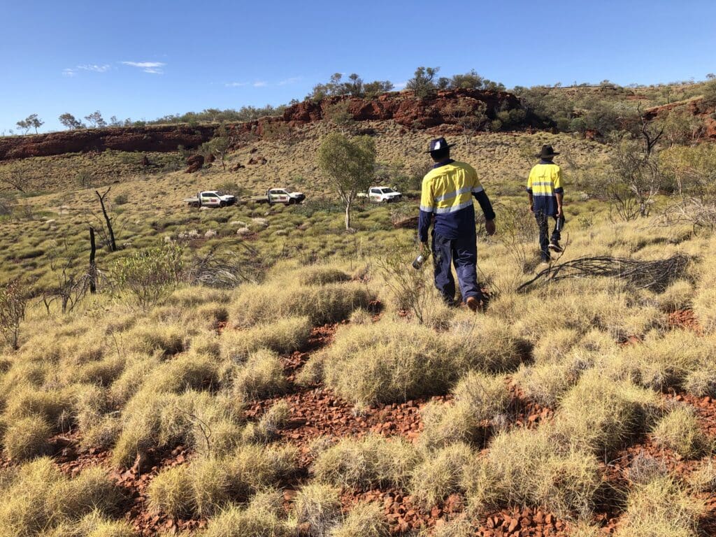 ACHM field team conducting archaeological site monitoring in a rocky red earth landscape