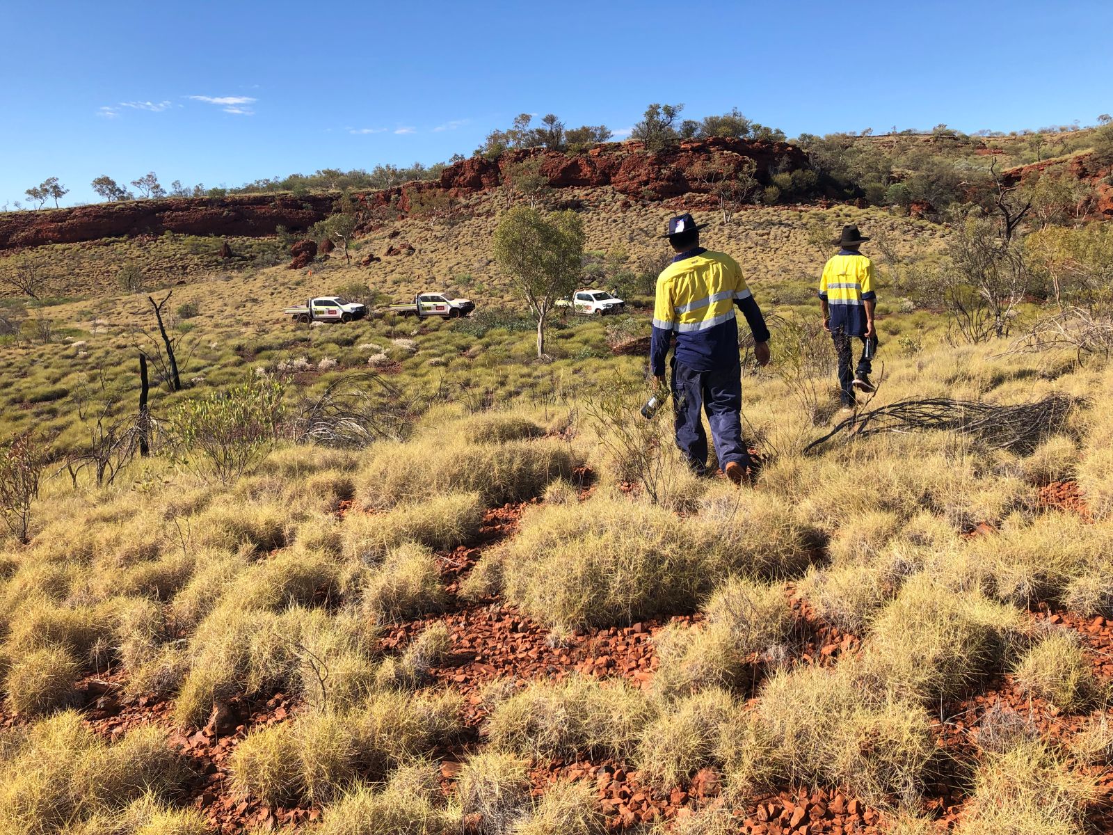 ACHM field team conducting archaeological site monitoring in a rocky red earth landscape